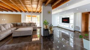 Een moderne woonkamer met een modulaire bank, houten plafond, groot televisiescherm en een glanzende betegelde vloer.