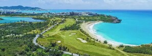 An aerial view of a coastal area with a golf course, beachfront, and buildings in the distance. - Lux Maho Reef Studio next to The Morgan Resort (Simpson Bay)