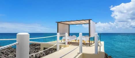 A beachside platform with a covered seating area, ropes, and a view of the ocean.