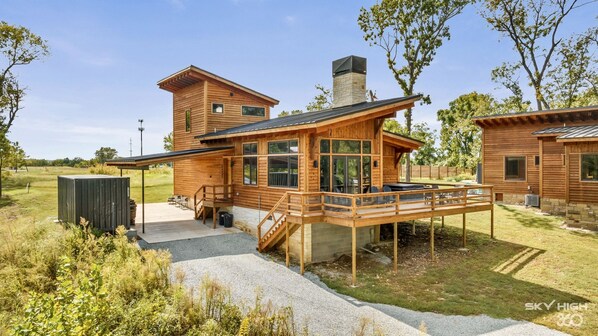 A modern wooden cabin with a deck, large windows, and a stone chimney. - Twin Retreat Cabin #2, Hot Tub, Near Battlefield Golf Course & Shangri La Resort (Afton)