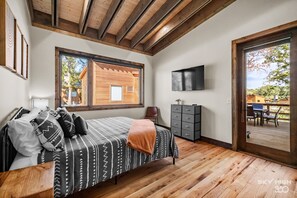 A bedroom with a bed, a TV, a wooden floor, and a large window. - Twin Retreat Cabin #2, Hot Tub, Near Battlefield Golf Course & Shangri La Resort (Afton)