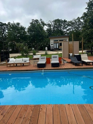 Una piscina con sillas de descanso y un edificio pequeño al fondo.