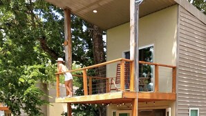 A two-story wooden house with a balcony, a small deck, and a pond in front. - The Walnut Villa at Selah Place (Athens)