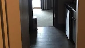 Ein enger Flur, der zu einem Raum führt, mit einer Tür links und einem Fenster mit Vorhängen rechts.
