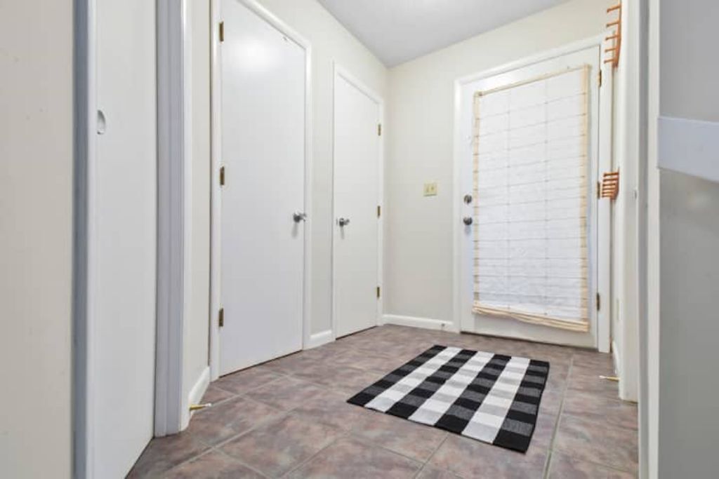Un couloir avec des portes blanches, un tapis à carreaux et une fenêtre avec des stores.