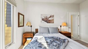 Ein Schlafzimmer mit einem Bett, zwei Nachttischen, einer Lampe, einem gerahmten Bild an der Wand und einer Tür.