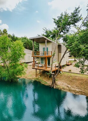 A two-story house with a deck overlooking a body of water, surrounded by trees.