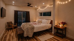 A bedroom with a bed, a chair, a bench, a bedside table with a bottle and flowers, and a window with curtains. - Villa 1 · Waterfront Villa, spacious with 2 balcony and beds (Athens)