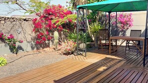 A wooden deck with a table and chairs, surrounded by a garden with pink flowers and a cactus. - Volcano Sunset View Villa in Corralejo-Tamaragua. (Corralejo City)