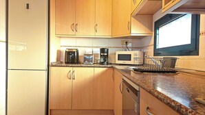 A compact kitchen with wooden cabinets, a refrigerator, a microwave, a coffee maker, and a dishwasher. - Volcano Sunset View Villa in Corralejo-Tamaragua. (Corralejo City)