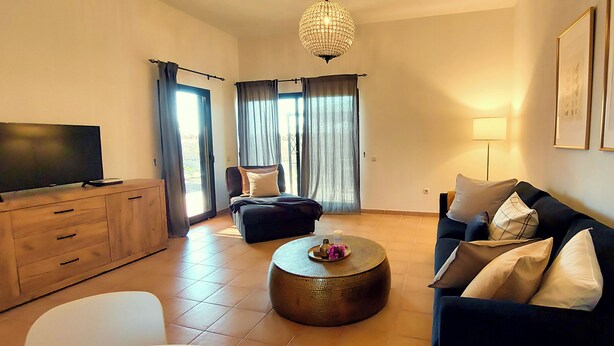 A modern living room with a flat-screen TV, a sofa, a round coffee table, and a chair. - Volcano Sunset View Villa in Corralejo-Tamaragua. (Corralejo City)
