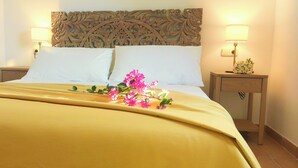 A bed with a yellow bedspread, two white pillows, and a decorative headboard. There are two bedside tables with lamps and a small flower arrangement. - Volcano Sunset View Villa in Corralejo-Tamaragua. (Corralejo City)