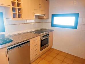Een keuken met een vaatwasser, oven en een raam met zonwering.