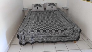 A small, neatly made bed with a patterned bedspread and two pillows with tree designs. - Studio La Vigie 3 (Deshaies)