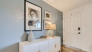 A hallway with a white console table, framed artwork, and a lamp.