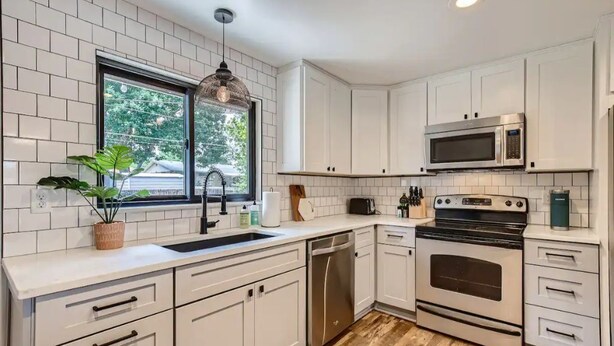 A modern kitchen with white cabinets, a stainless steel dishwasher, a built-in oven, and a microwave.