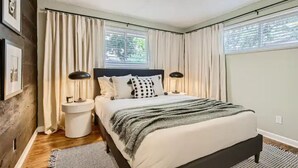 A bedroom with a bed, two bedside tables, a lamp, and a window with curtains.