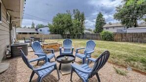 A backyard patio with a fire pit and four Adirondack chairs.