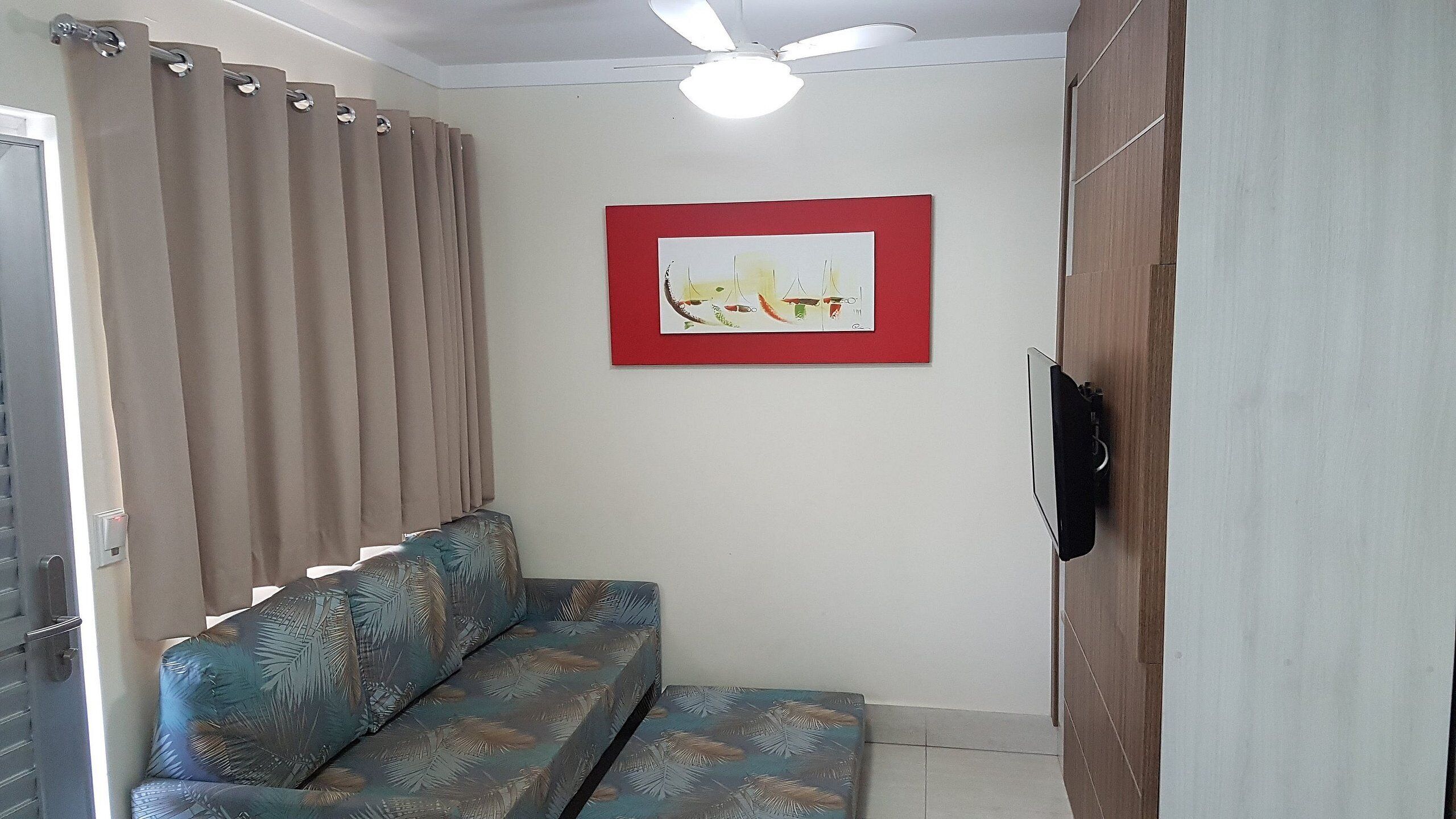 A room with a sofa, a ceiling fan, a TV mounted on the wall, and a red-framed picture.