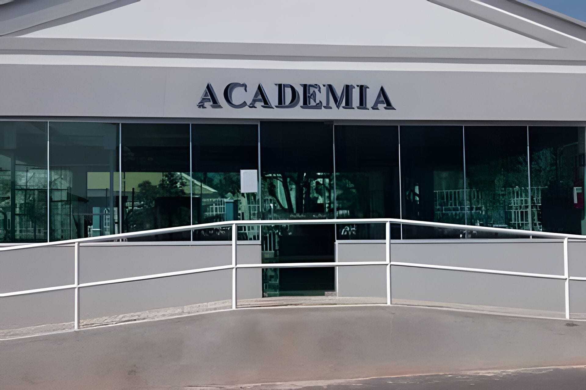 The exterior of an academy building with a modern design, large glass windows, and a white railing in front.