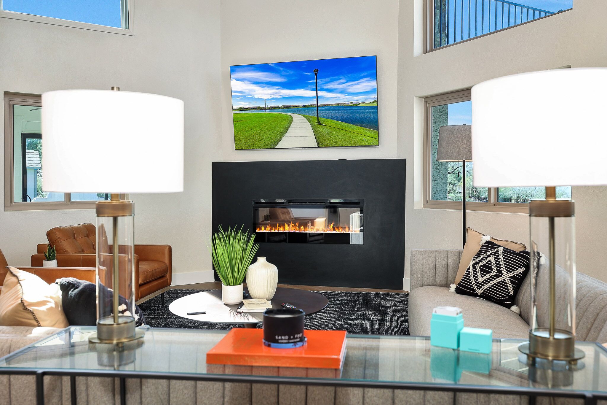 A modern living room with a fireplace, a large TV mounted above it, and a glass coffee table with decorative items.