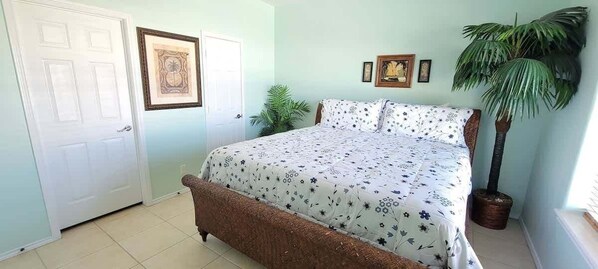 Un dormitorio con cama, puerta, un cuadro enmarco y una planta en maceta.