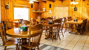 A wooden interior with multiple dining tables and chairs, ceiling fans, and a window with blinds.