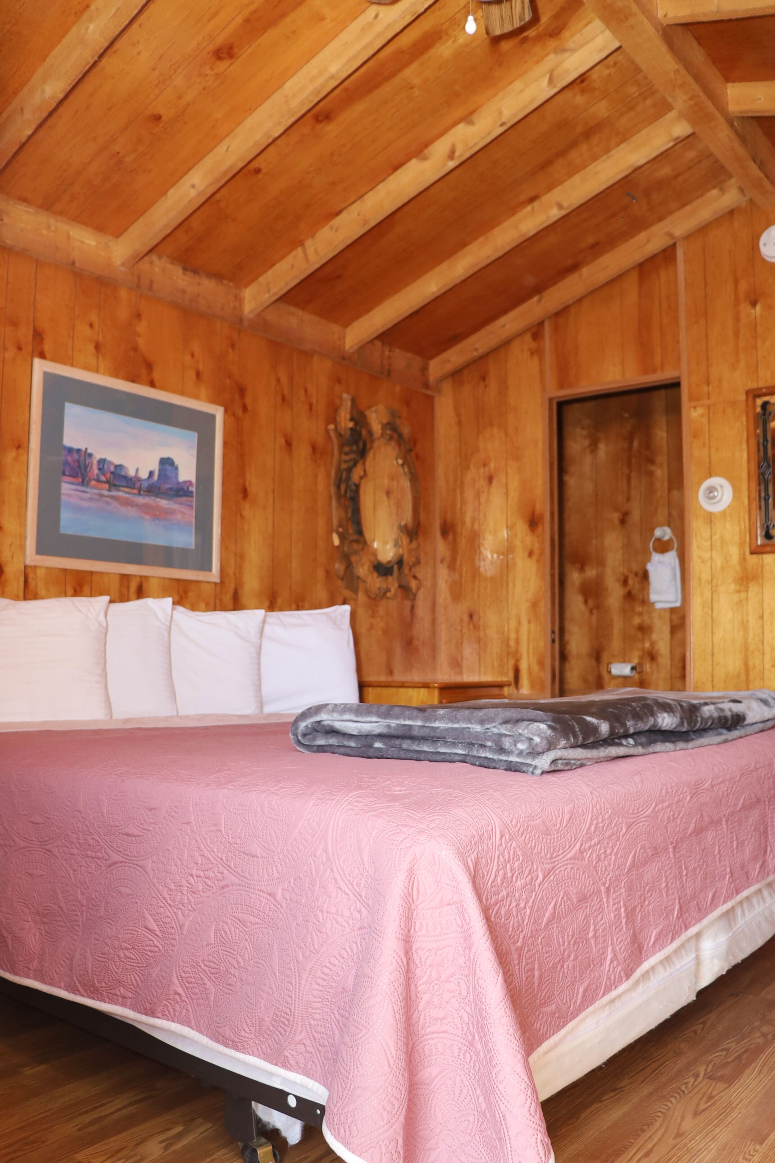 Quarto de cabana de madeira com uma cama, um quadro na parede e uma porta.