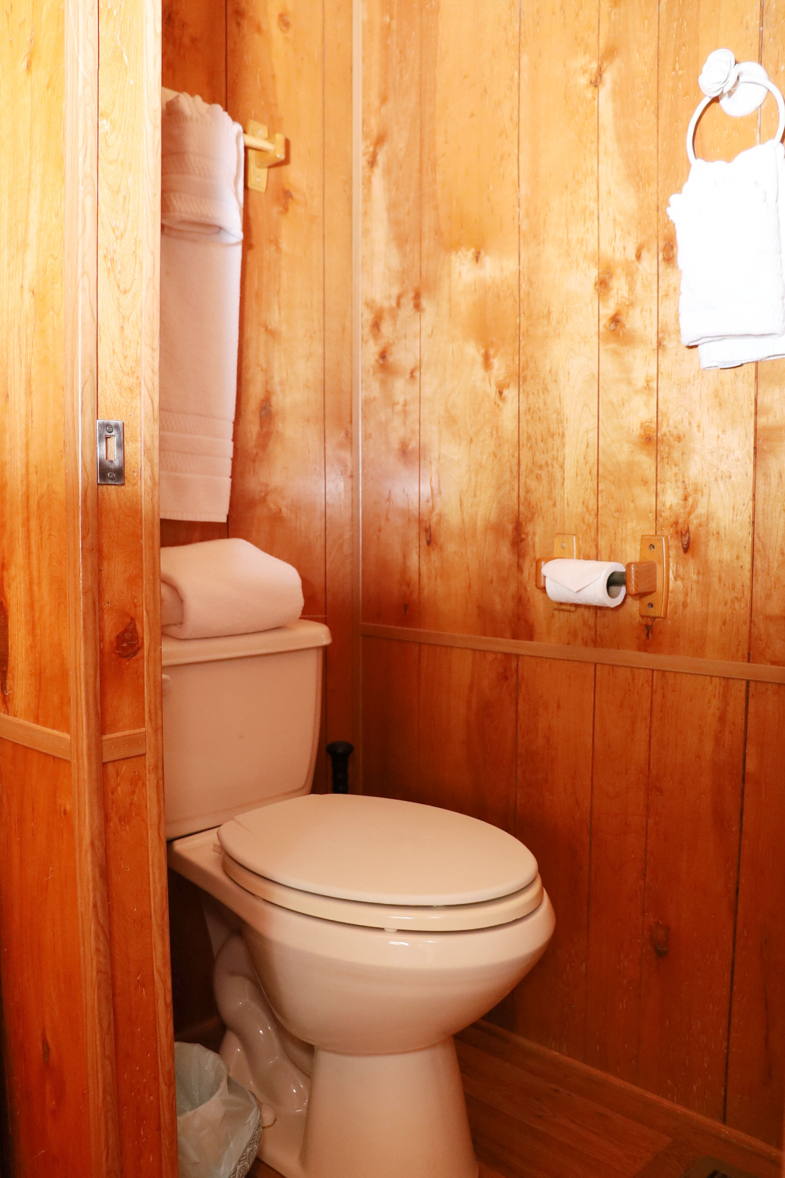 A wooden bathroom with a toilet, a towel rack, and a toilet paper holder.