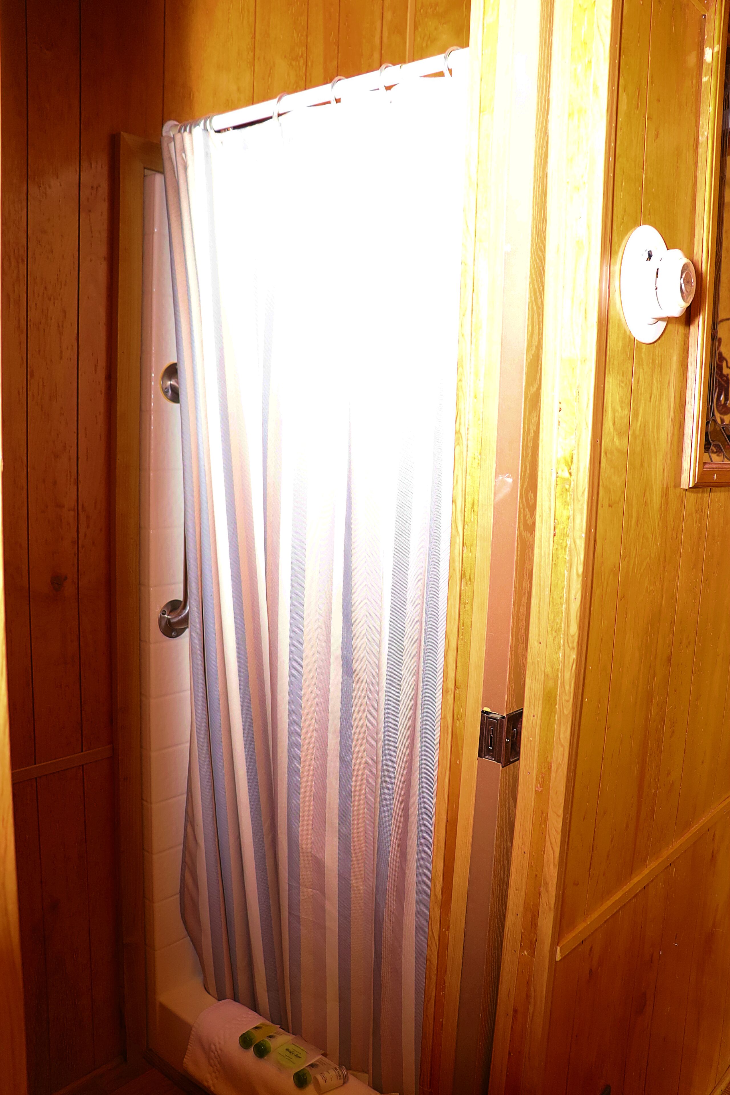 Ett badrum med träpanel, en duschdraperi, en handdukshängare och en dörr med ett handtag.