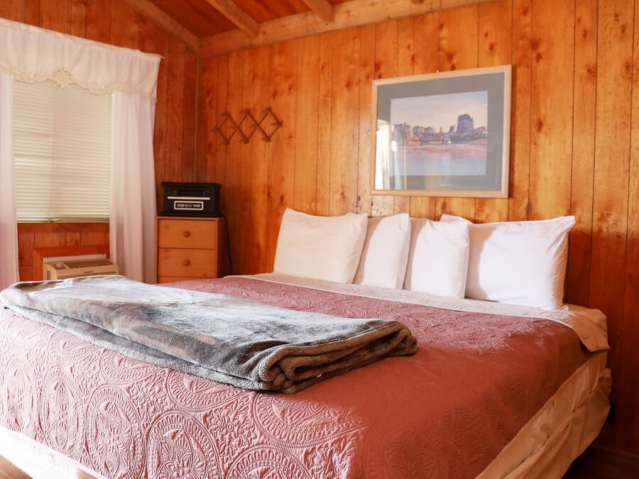 A wooden-paneled bedroom with a bed, a dresser, and a framed picture on the wall.