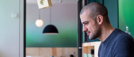 A man working at a table with a laptop, in a room with modern pendant lighting and a green wall.