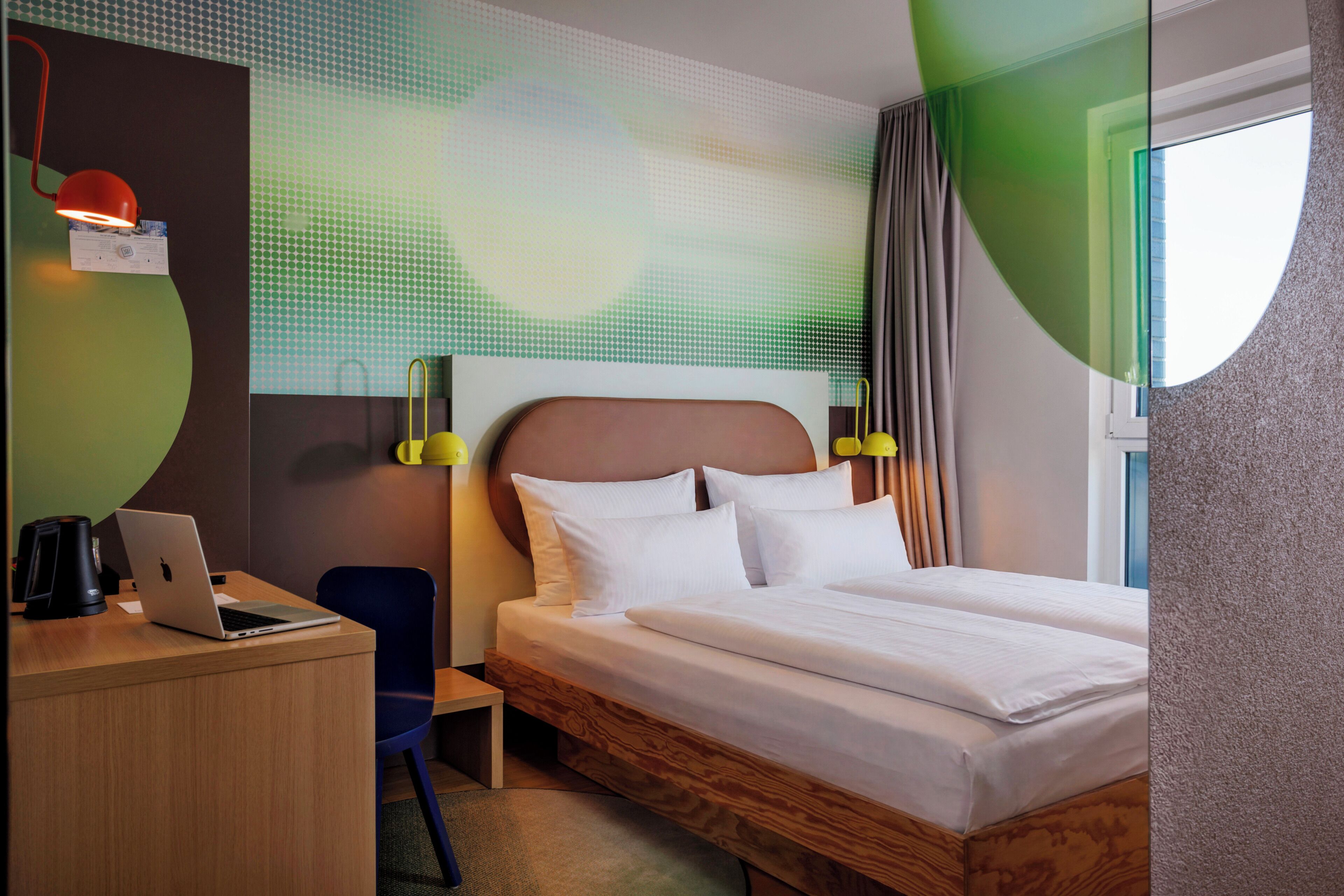 Ein Hotelzimmer mit Bett, Schreibtisch, Laptop und Blick ins Freie.