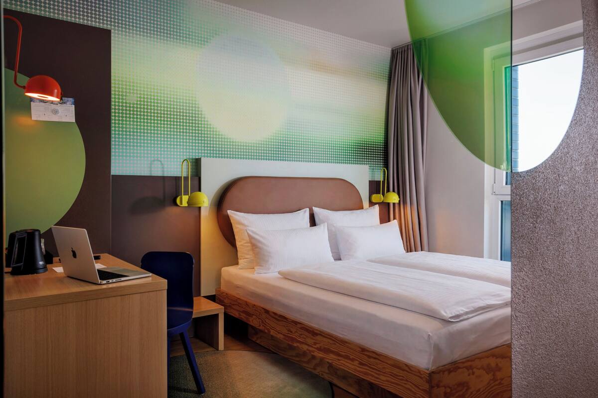 Habitación de hotel con cama, escritorio, computadora portátil y vistas al exterior.