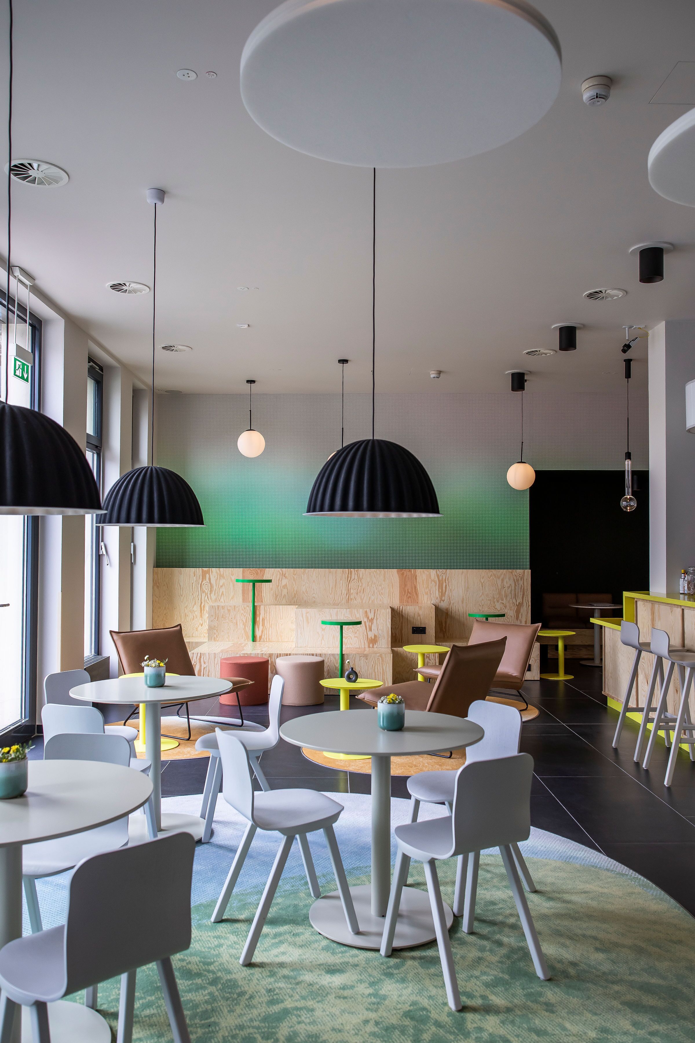 A modern interior with round tables and chairs, pendant lighting, and a green wall.