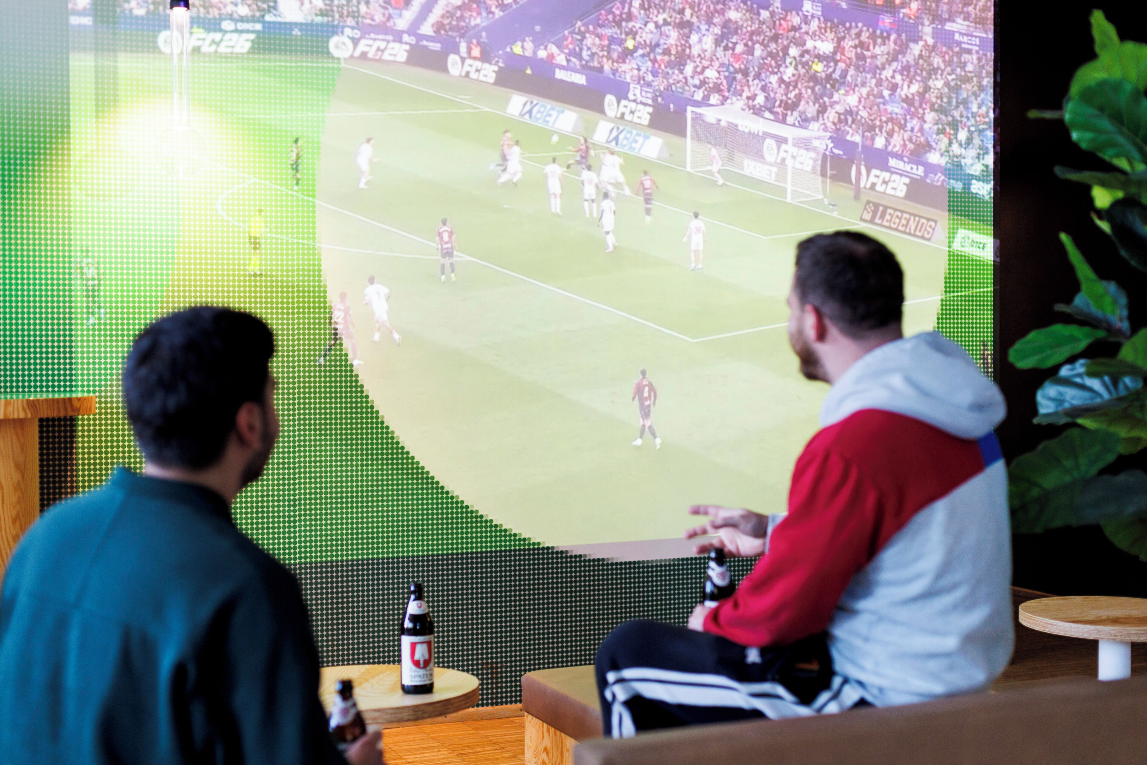 Two individuals watching a large screen displaying a soccer match.