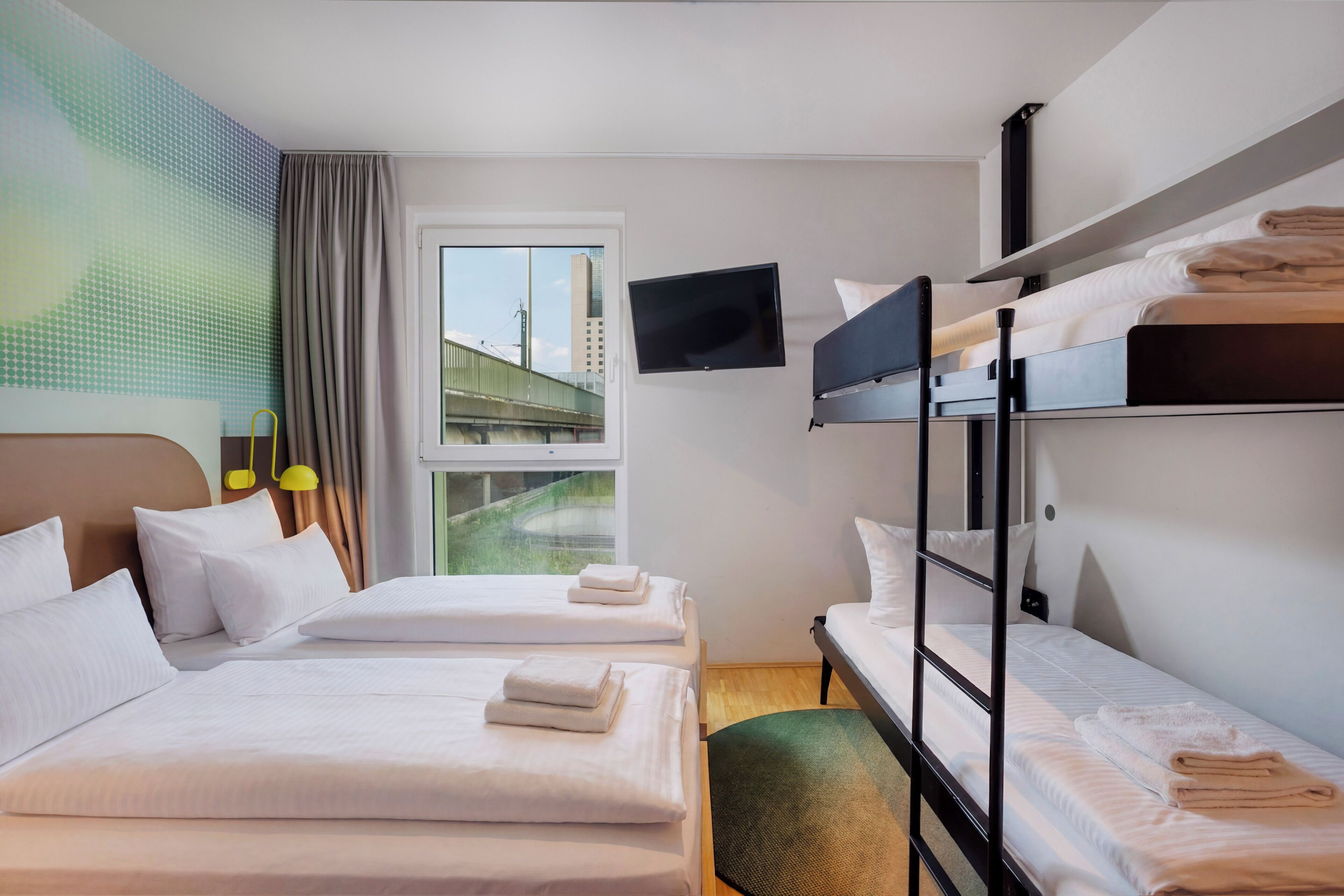 A hotel room with two beds, a TV, a window with a view of a bridge, and a green wall.