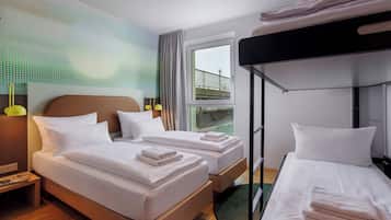 A hotel room with two beds, a bunk bed, a window with a view, and a nightstand with a lamp.
