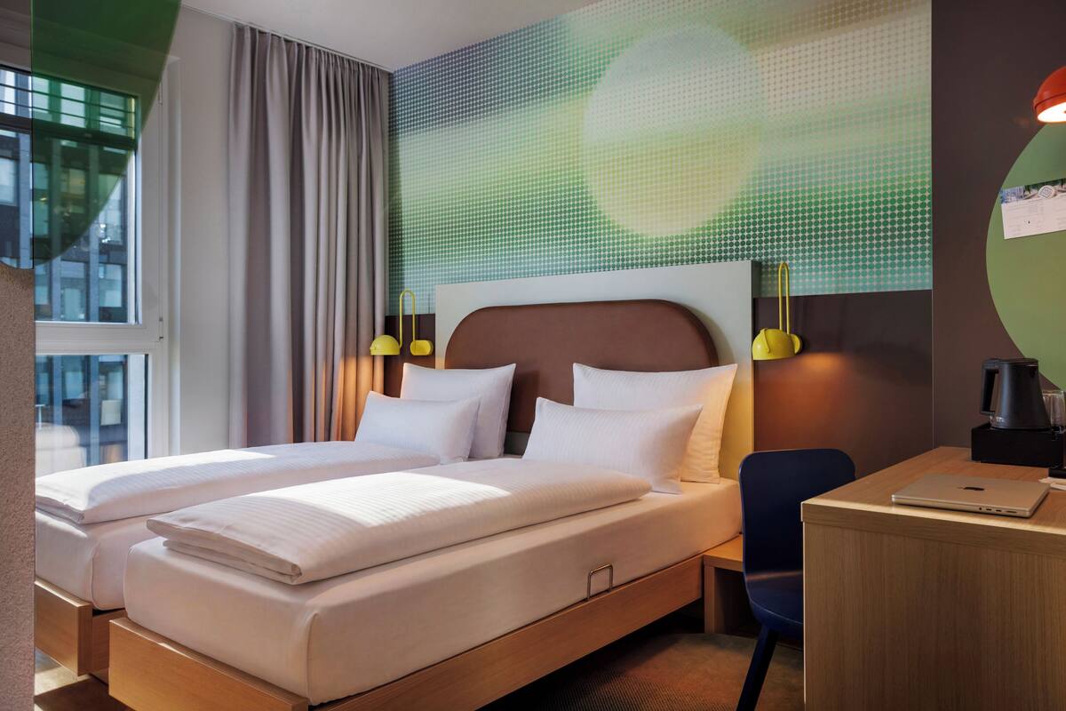 Habitación de hotel con dos camas, un escritorio, una silla y vistas a la ciudad.