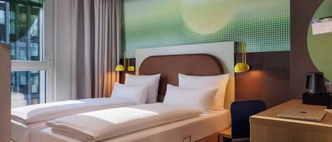 A hotel room with two beds, a desk, a chair, and a view of the city.