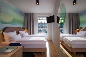 A hotel room with two beds, a TV, a desk with a laptop, and a large window. - LyvInn Hotel Frankfurt   (Frankfurt)