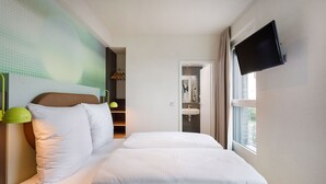 A modern hotel room with a large bed, a television mounted on the wall, and a view of the city through the window. - LyvInn Hotel Frankfurt   (Frankfurt)