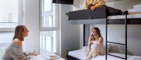 Une chambre avec un lit superposé, un téléviseur fixé au-dessus du lit du haut, une fenêtre avec des stores et une vue sur l’extérieur.