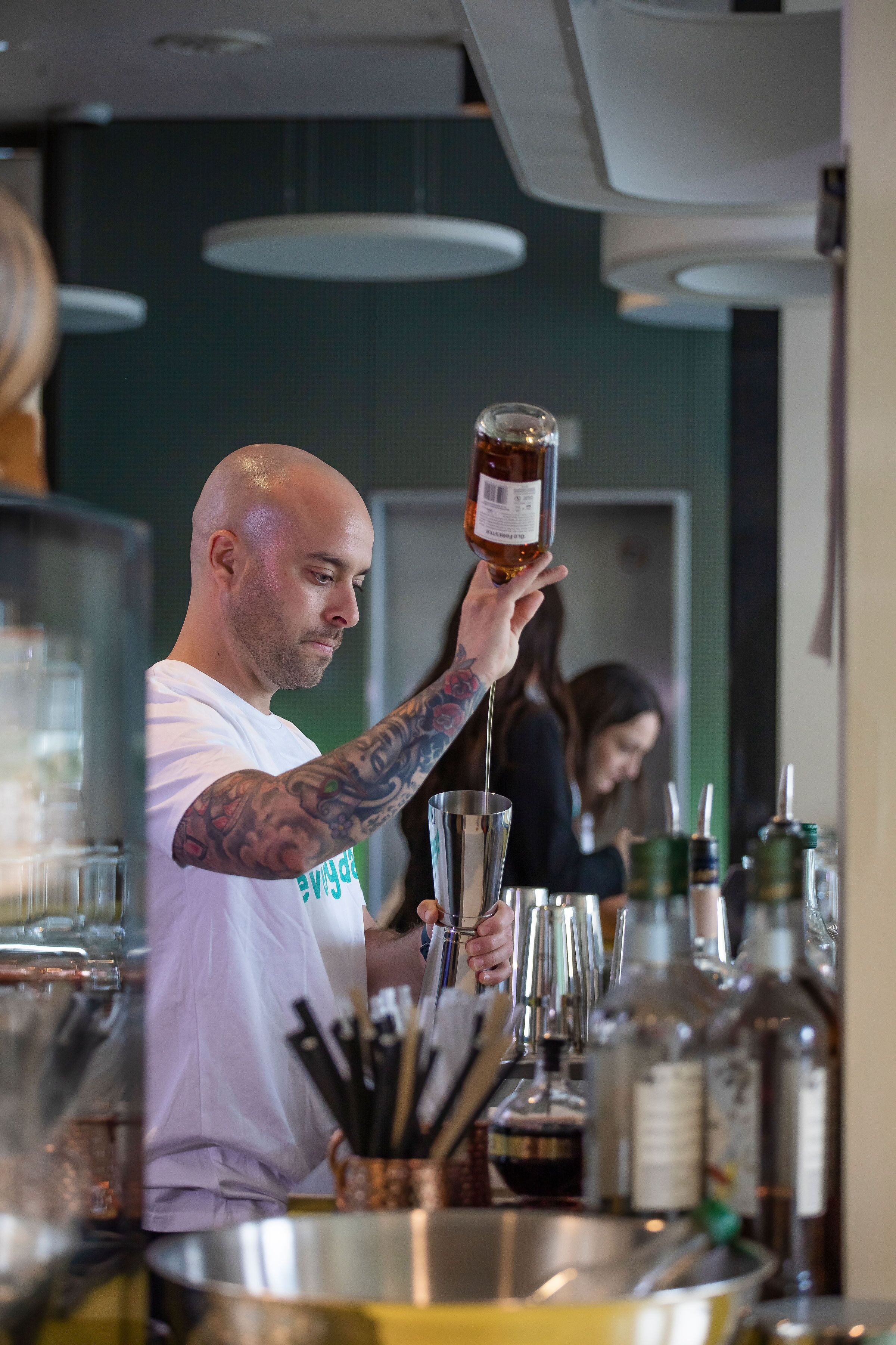 A bartender preparing a drink at a bar with various bottles and glasses.