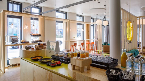 A modern kitchen with a central island, various food items, and a seating area with orange chairs. - LyvInn Hotel Frankfurt   (Frankfurt)