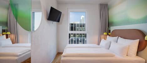 A hotel room with a large bed, a TV mounted on the wall, a window with a city view, and a wooden floor.