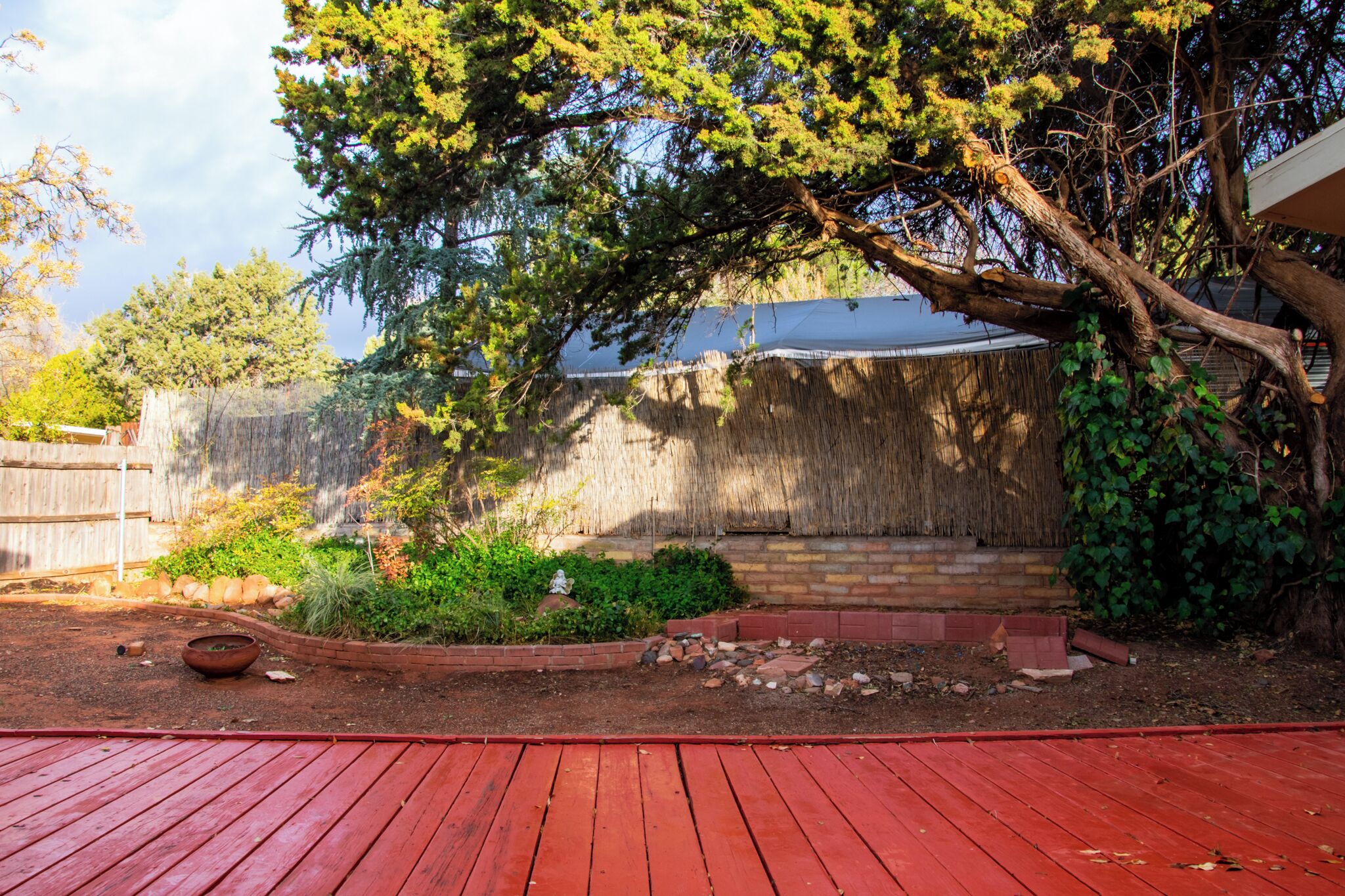 A backyard with a red deck, a thatched wall, and a variety of plants.