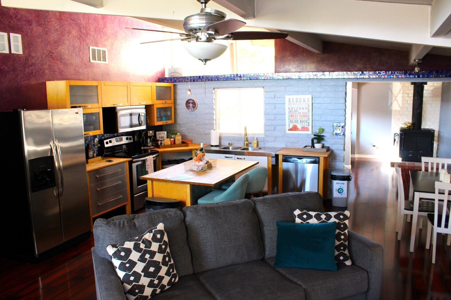 A compact kitchen with a refrigerator, microwave, and stove. There is a dining area with a table and chairs, and a sofa with patterned cushions.