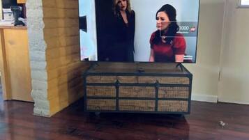 Un televisor sobre un mueble de madera en una habitación con pared de ladrillo y equipo de aire acondicionado.