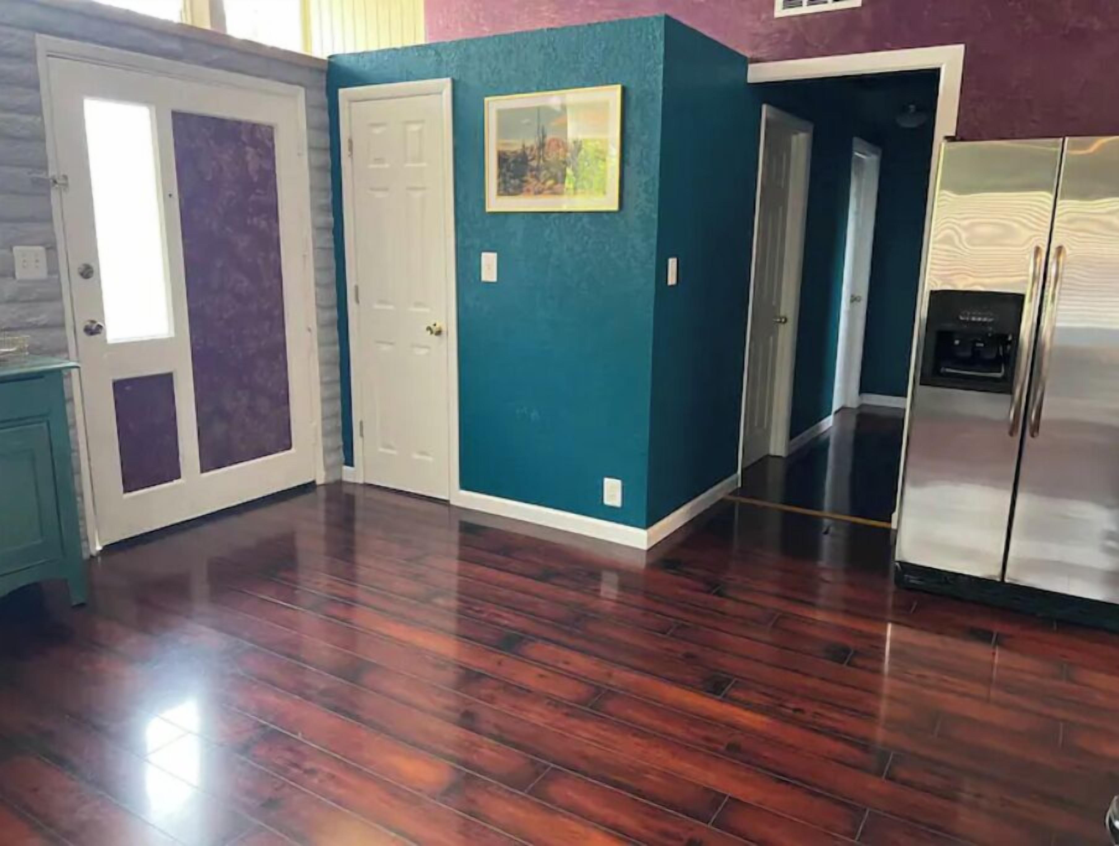 A kitchen with teal walls, a stainless steel refrigerator, and wooden flooring.